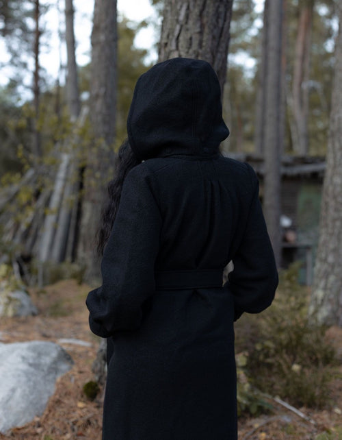 Person wearing a black hooded coat standing in a forest
