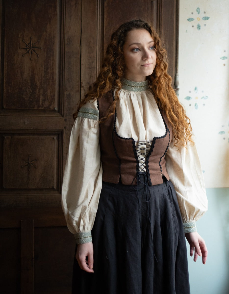 Woman in a historical costume standing in a room with wooden paneling.