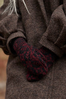 A close-up of a person wearing a dark brown textured coat and a dark red and black patterned knit glove, with hands tucked into the coat pocket.