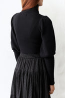 Woman wearing a black bishop sleeves pullover against a white background