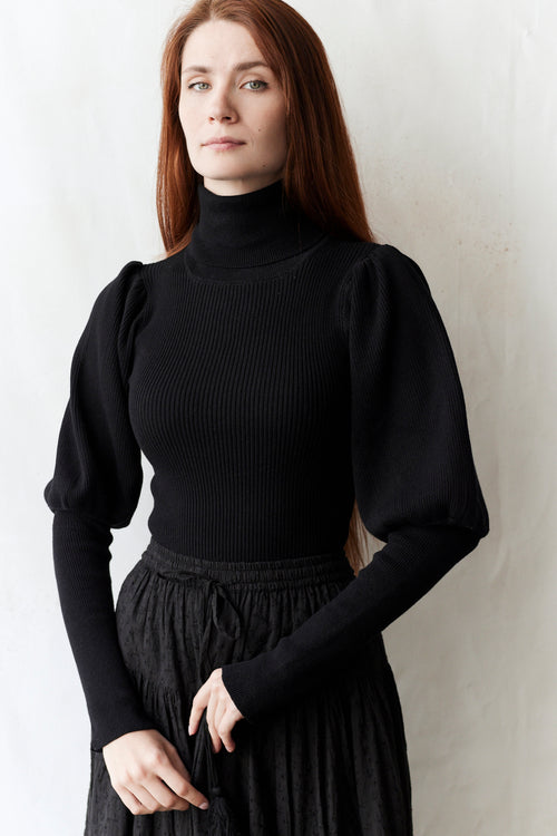 Woman wearing a black bishop sleeves pullover against a white background