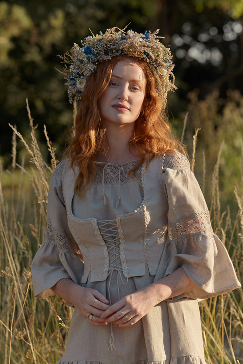 Woman in a natural linen dress and linen corset with linen lace standing among trees