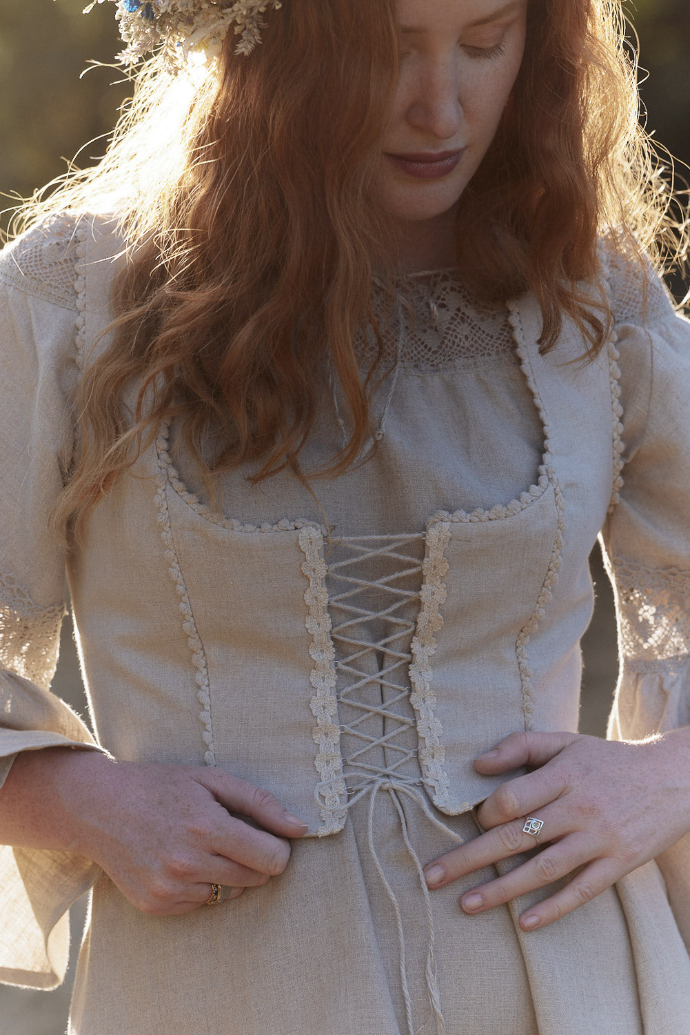 Woman in a natural linen dress and linen corset with linen lace standing among trees