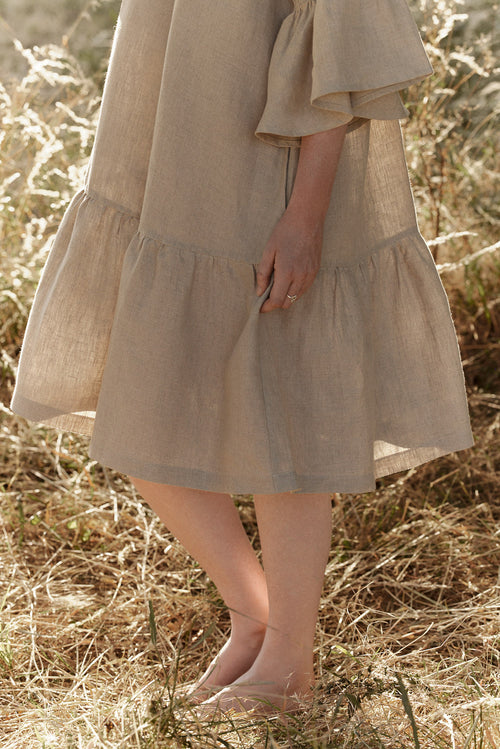 Woman in a natural linen dress with linen lace standing among trees