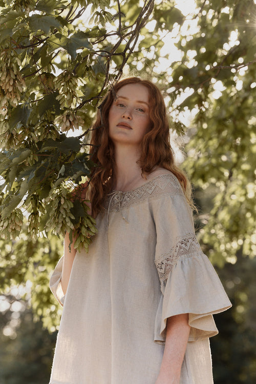 Woman in a natural linen dress with linen lace standing among trees