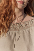 Person wearing a linen shoulder drop off blouse with lace details in a natural setting