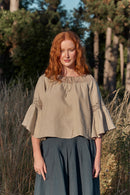 Woman with red hair wearing a linen shoulder drop off blouse with lace details in a natural setting