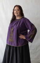 Plus size Woman wearing a purple blouse with embroidery against a white background