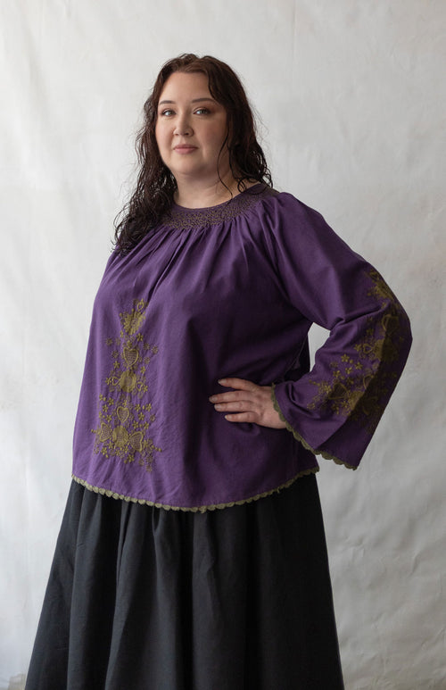 Plus size Woman wearing a purple blouse with embroidery against a white background