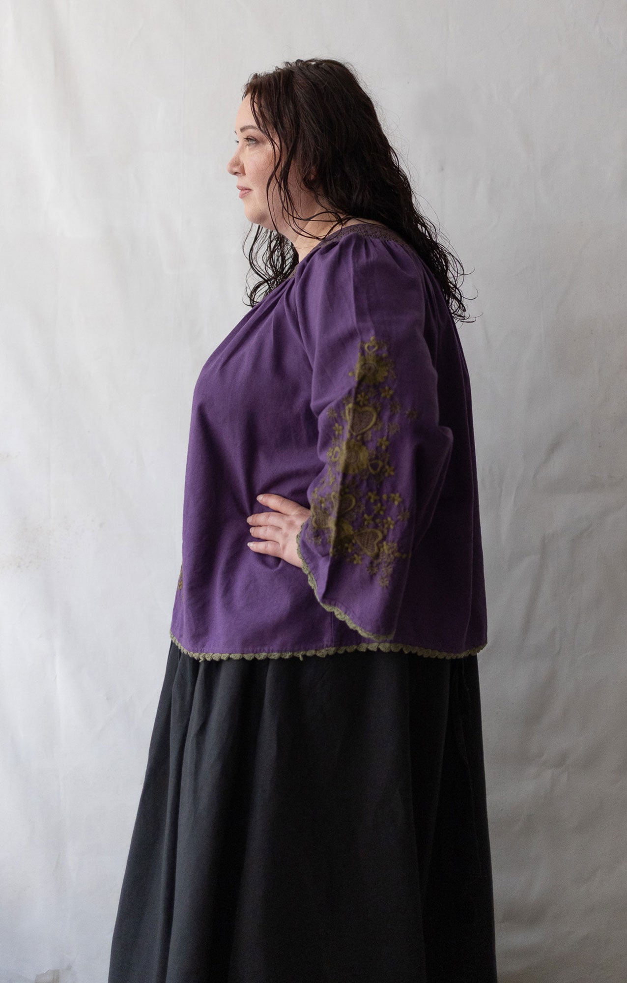 Plus size Woman wearing a purple blouse with embroidery against a white background