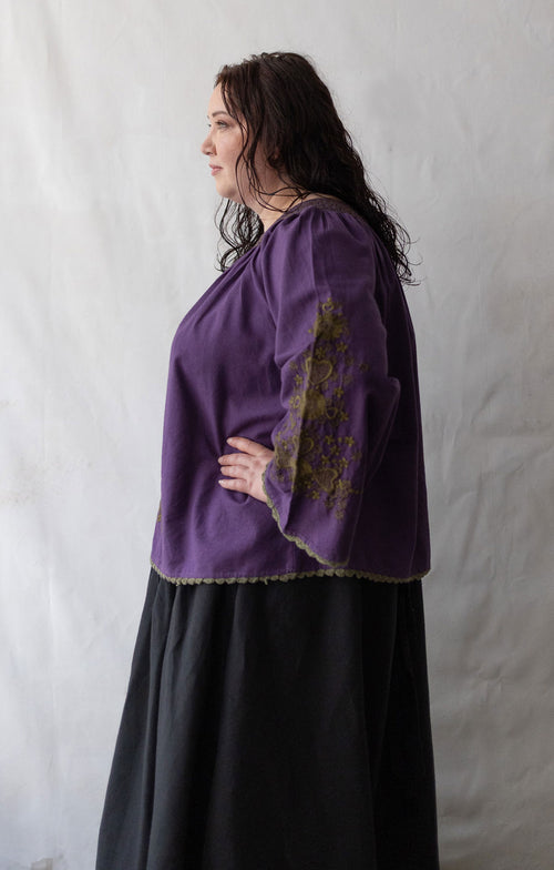 Plus size Woman wearing a purple blouse with embroidery against a white background