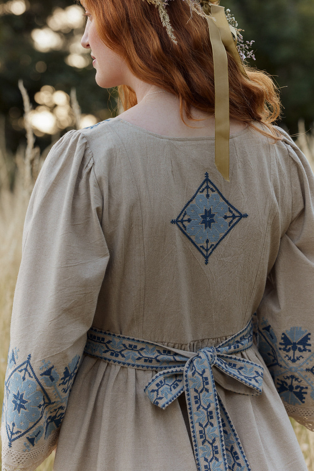 Person wearing a beige dress with blue embroidery in an outdoor setting