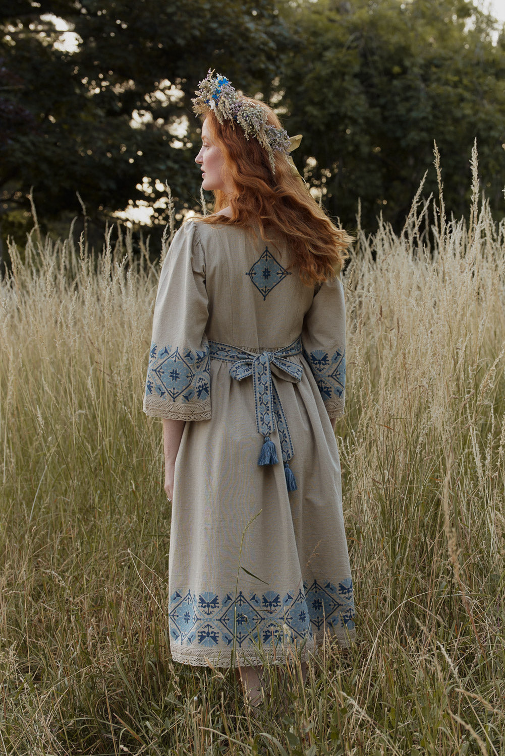 Woman in a traditional dress with blue patterns standing in a field.