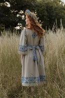 Woman in a traditional dress with blue patterns standing in a field.