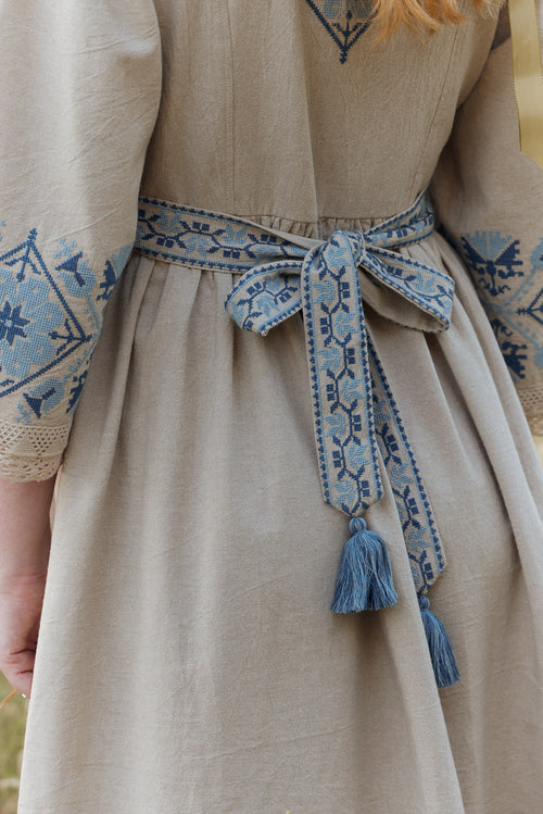 Beige dress with blue embroidery and tassels on a blurred background