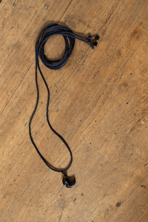 A black braided cord necklace with a small black bead pendant, laid out on a rustic wooden surface.
