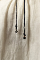 Close-up of a cream-colored linen garment with black drawstrings ending in small star-shaped metal charms.