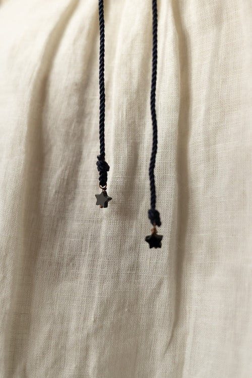 Close-up of a cream-colored linen garment with black drawstrings ending in small star-shaped metal charms.