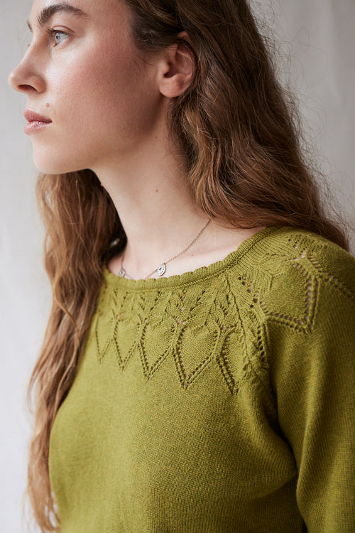 Woman wearing a green sweater with intricate lace detailing on a neutral background