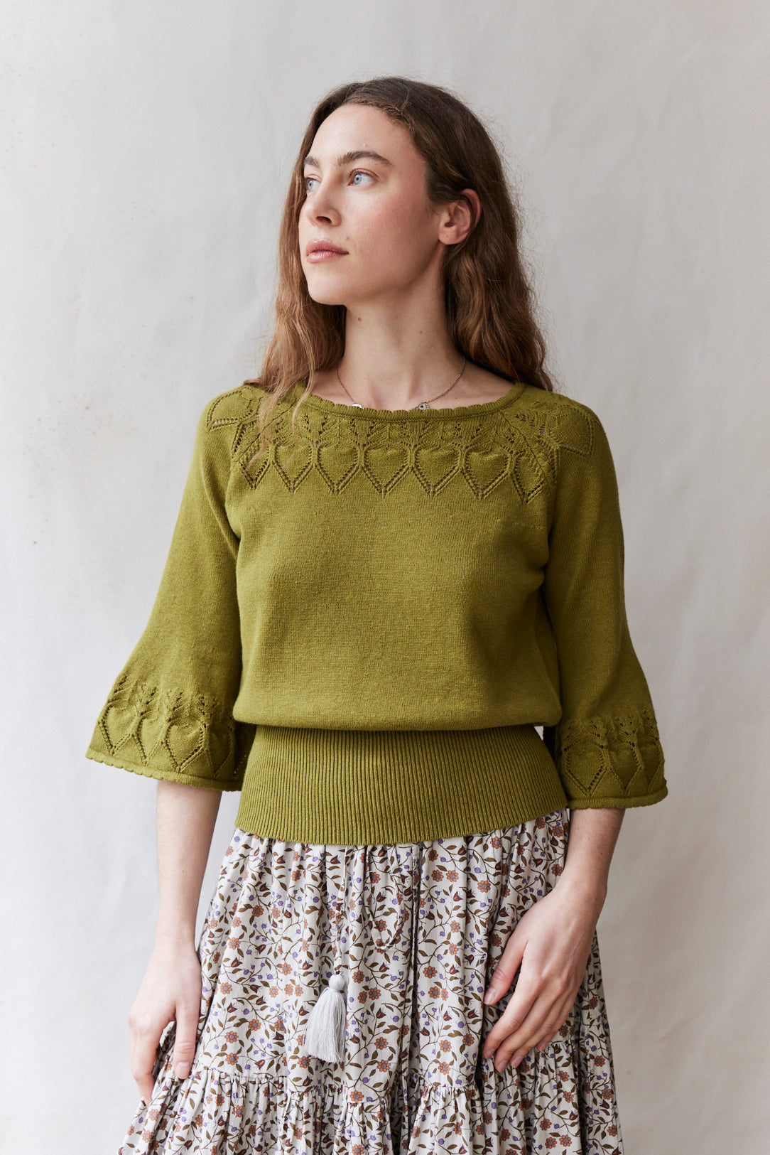 Woman wearing a green sweater with a patterned skirt against a plain background