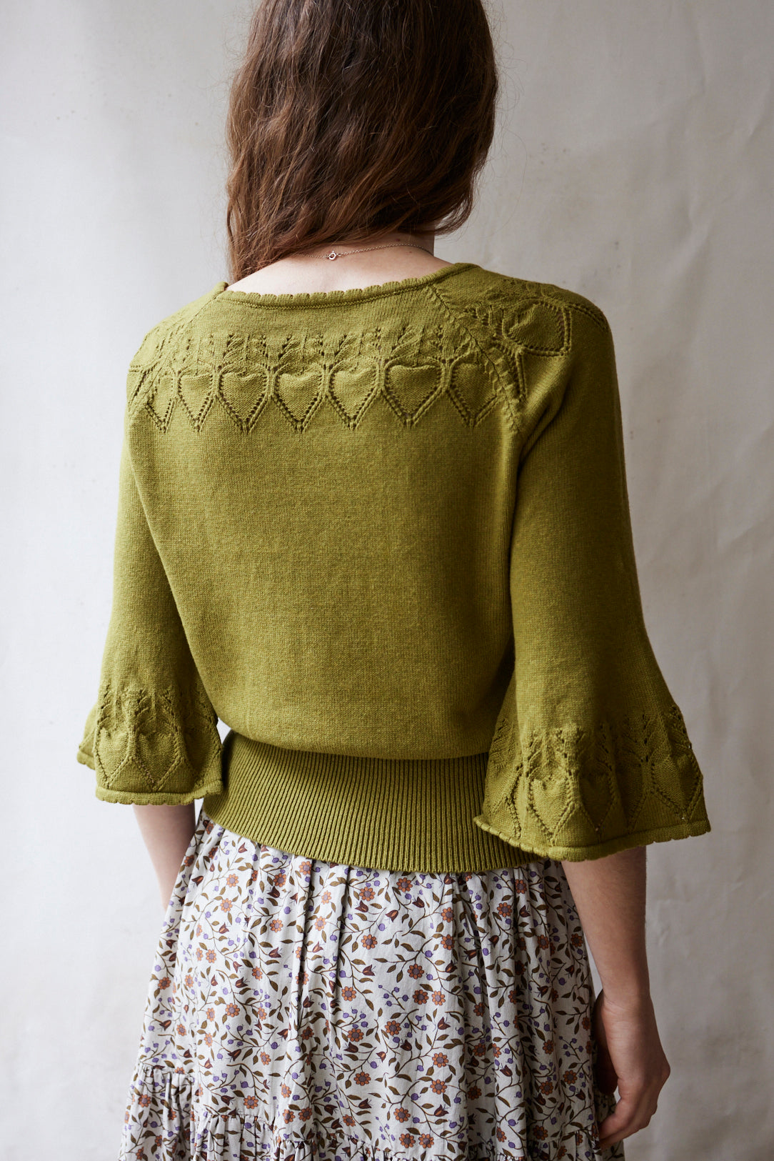 Person wearing a green knitted cardigan with heart patterns on a plain background