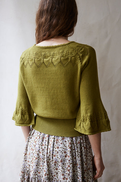 Person wearing a green knitted cardigan with heart patterns on a plain background