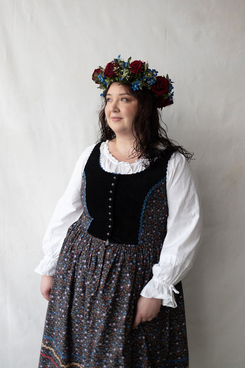 Plus size person wearing a traditional outfit with a floral headpiece against a plain background