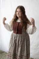 Woman wearing a historical outfit with a brown vest and floral skirt against a white background