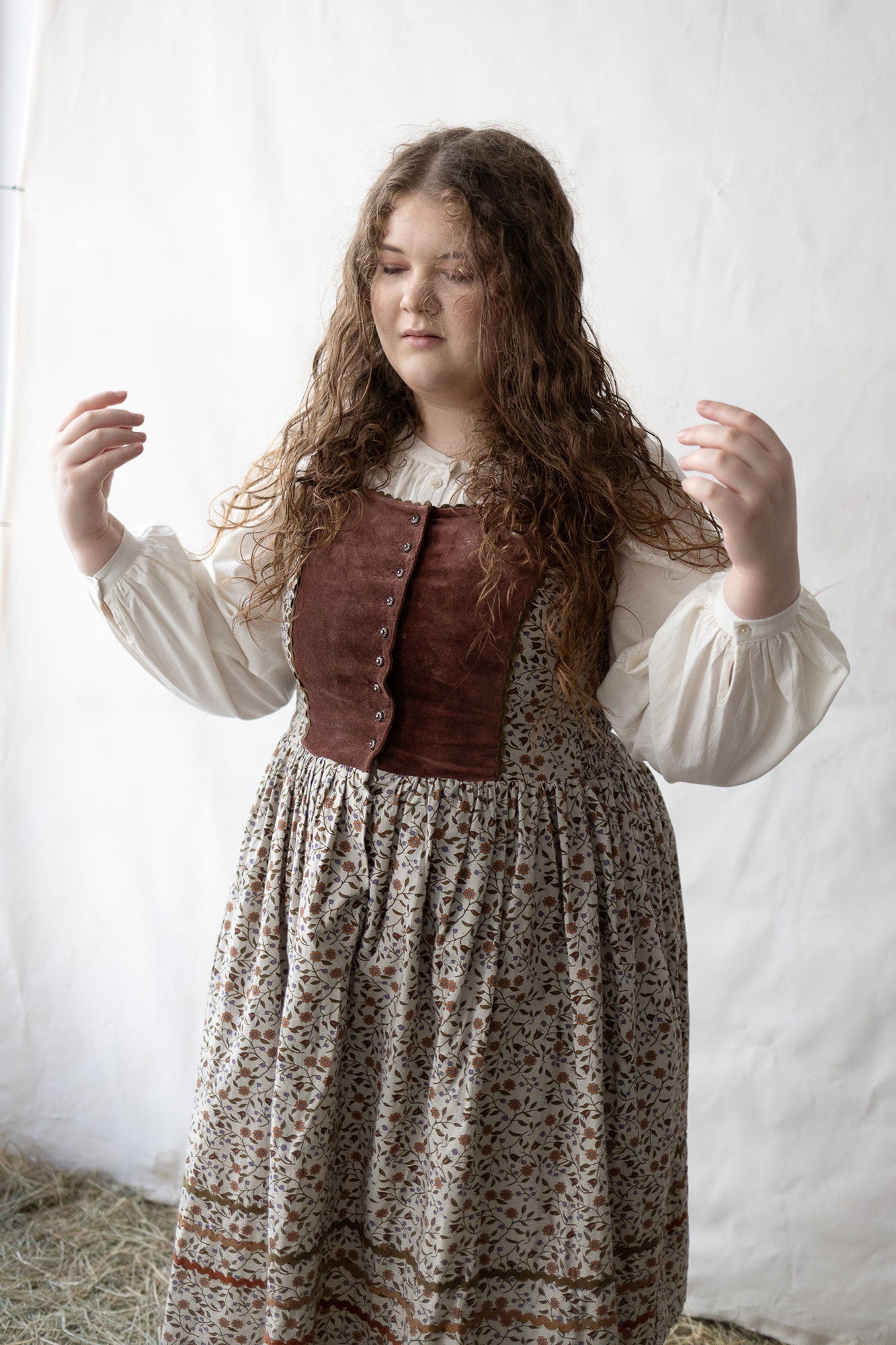 Woman wearing a historical outfit with a brown vest and floral skirt against a white background