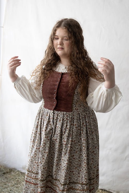 Woman wearing a historical outfit with a brown vest and floral skirt against a white background