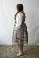 Person wearing a traditional outfit with a white blouse and patterned skirt on a white background.
