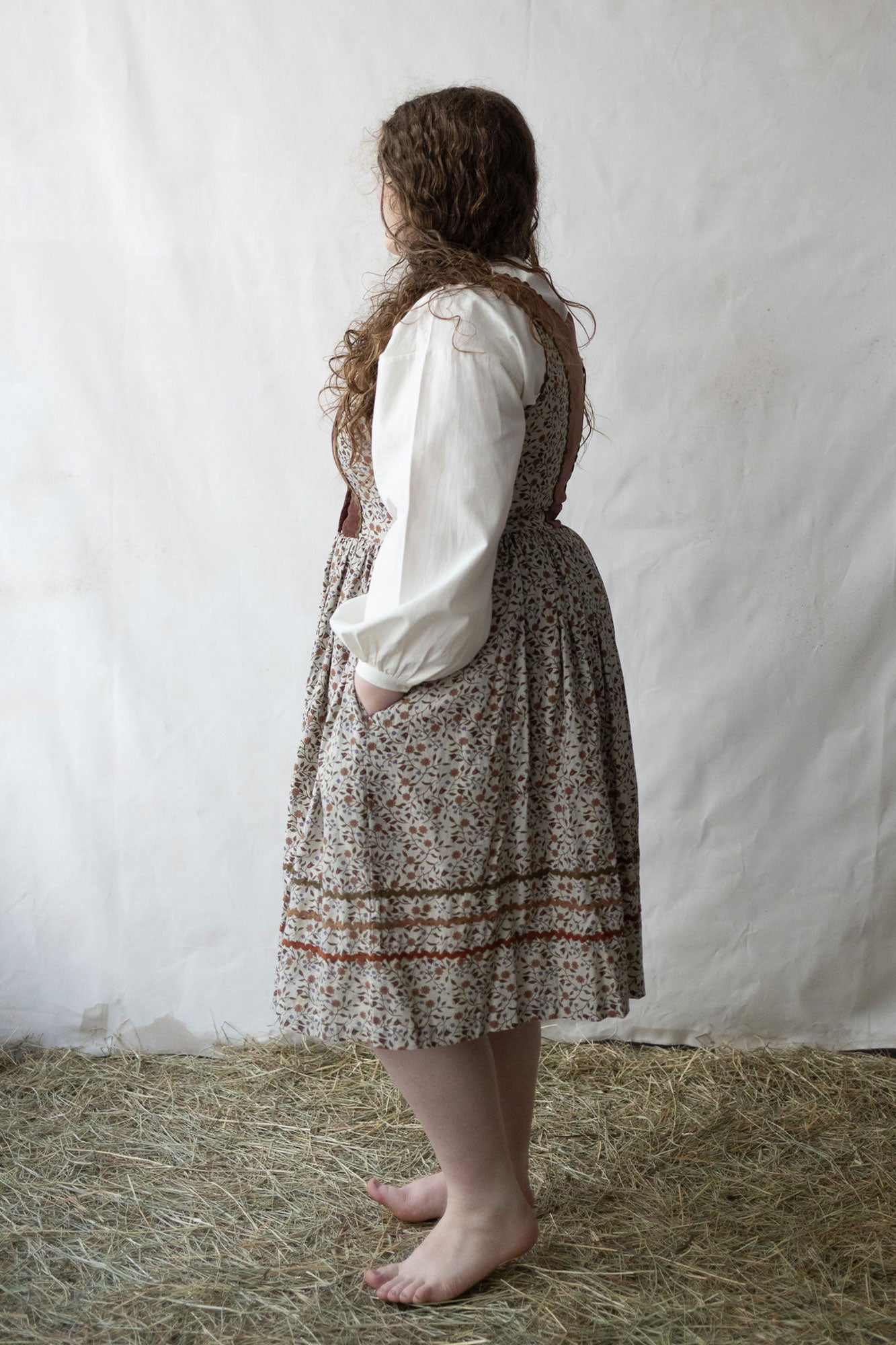 Person wearing a traditional outfit with a white blouse and patterned skirt on a white background.
