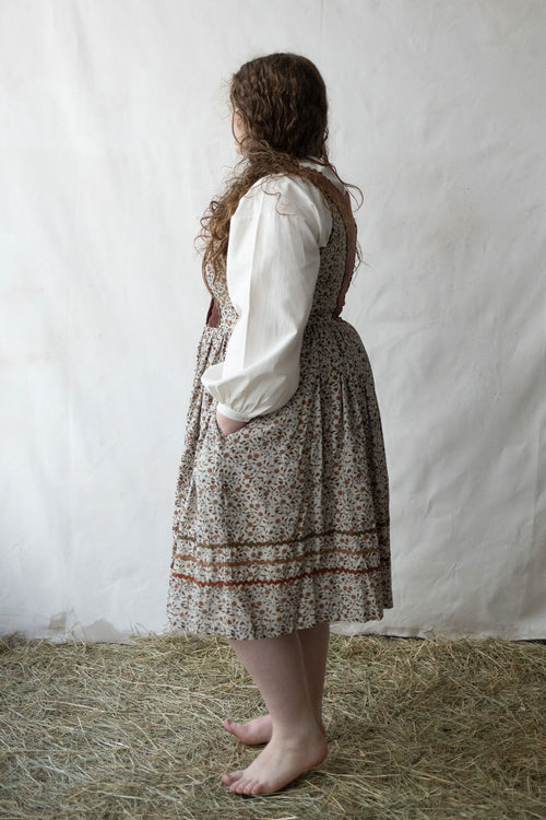 Person wearing a traditional outfit with a white blouse and patterned skirt on a white background.