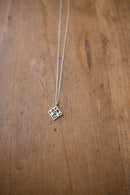 A silver geometric pendant necklace on a delicate chain, displayed on a rustic wooden surface.