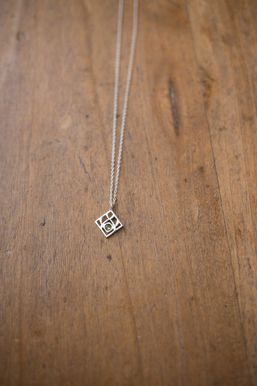 A silver geometric pendant necklace on a delicate chain, displayed on a rustic wooden surface.