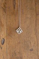 A delicate silver geometric pendant necklace with a small central gold circle, hanging against a rustic wooden plank background.