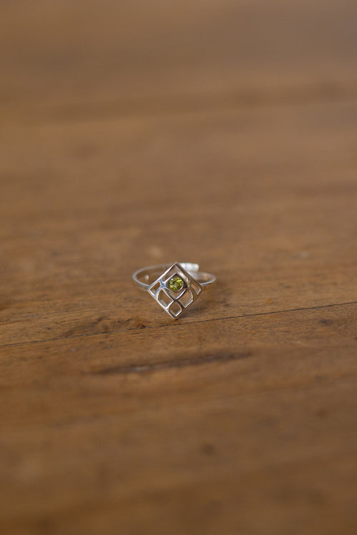 A silver geometric ring with a small green gemstone in the center, resting on a rustic wooden surface.
