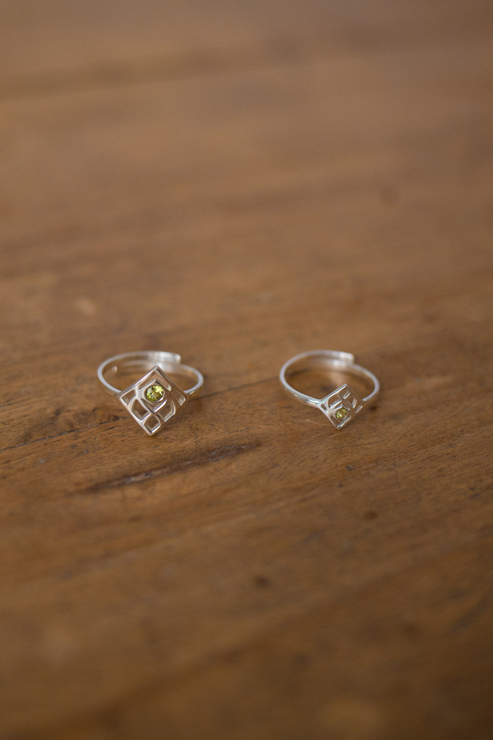 A pair of silver geometric hoop earrings with small yellow gemstone accents, resting on a rustic wooden surface.