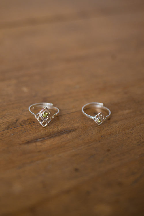 A pair of silver geometric hoop earrings with small yellow gemstone accents, resting on a rustic wooden surface.