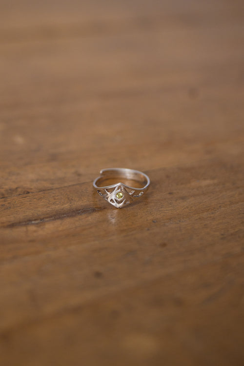 A delicate silver ring with a small central yellow gemstone and subtle side details, resting on a warm, blurred wooden surface.