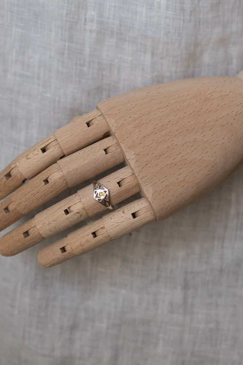 A silver ring with a heart-shaped crystal pendant displayed on a wooden mannequin hand against a textured gray fabric background.