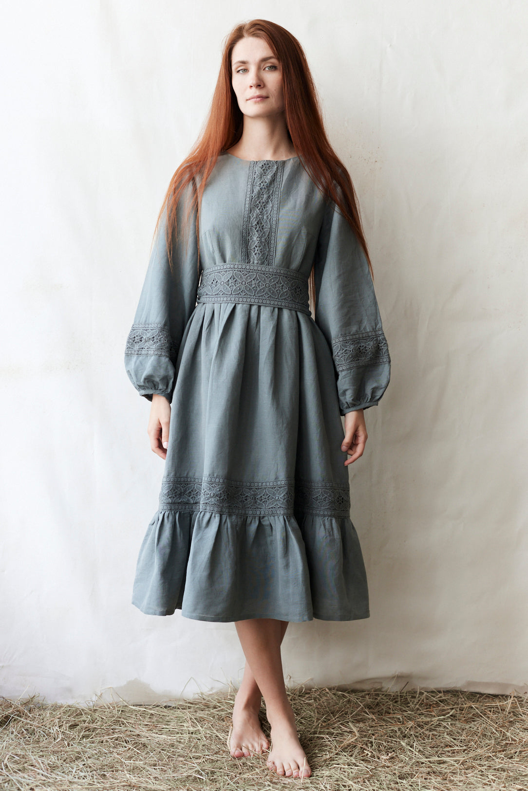 Woman wearing a gray dress with intricate patterns against a plain background