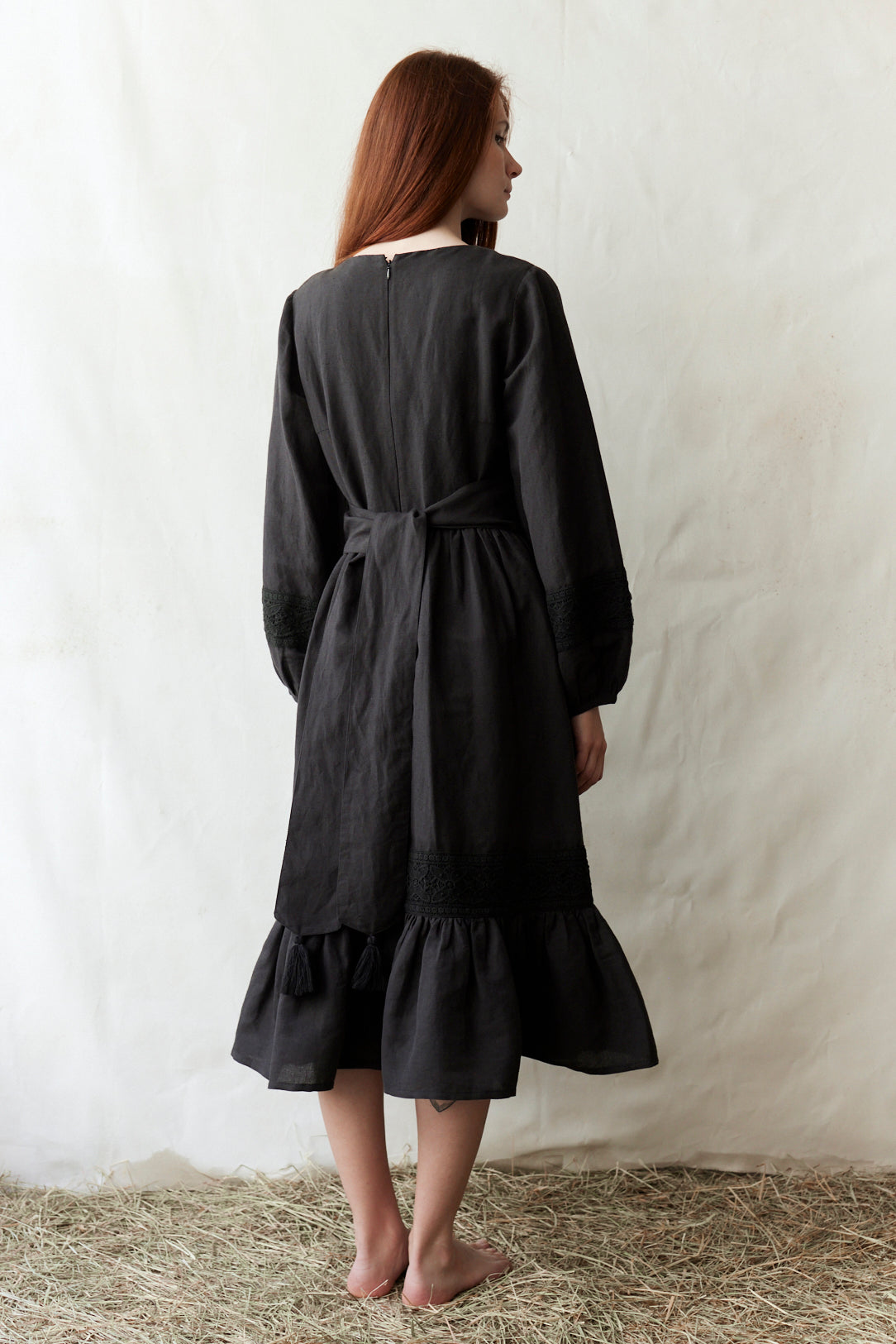 Woman wearing a black dress standing on straw with a white background