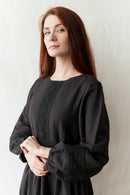 Woman wearing a black dress with intricate detailing against a plain background
