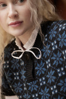 Close-up of a woman wearing a dark navy and blue patterned knit sweater with a cream ruffled collar and bow detail.