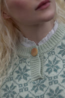 Close-up of a model wearing a light green and white patterned knit sweater with a ruffled white collar and a single wooden button.