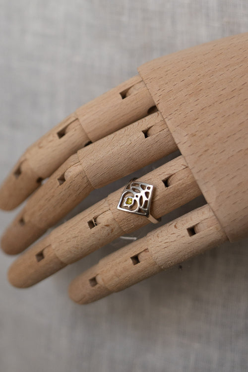 A silver ring with a cow print design and a small yellow gemstone, displayed on a wooden mannequin hand against a neutral gray background.