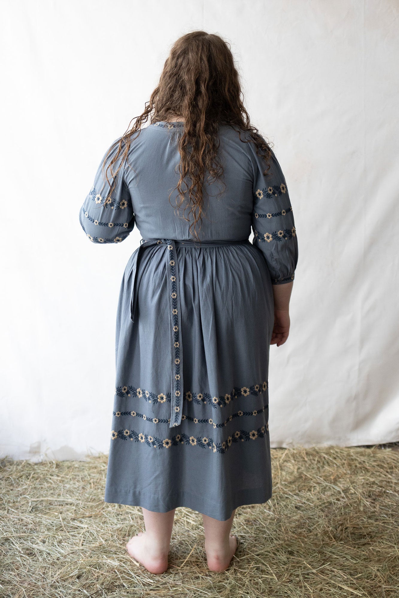 Plussize woman wearing a blue dress with floral details against a plain background