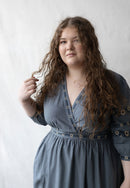 Plussize woman wearing a blue dress with floral details against a plain background