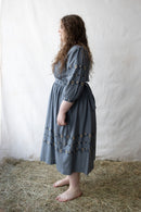 Plussize woman wearing a blue dress with floral details against a plain background